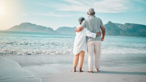 A retired couple holds each other as they stand on the beach and enjoy retirement.